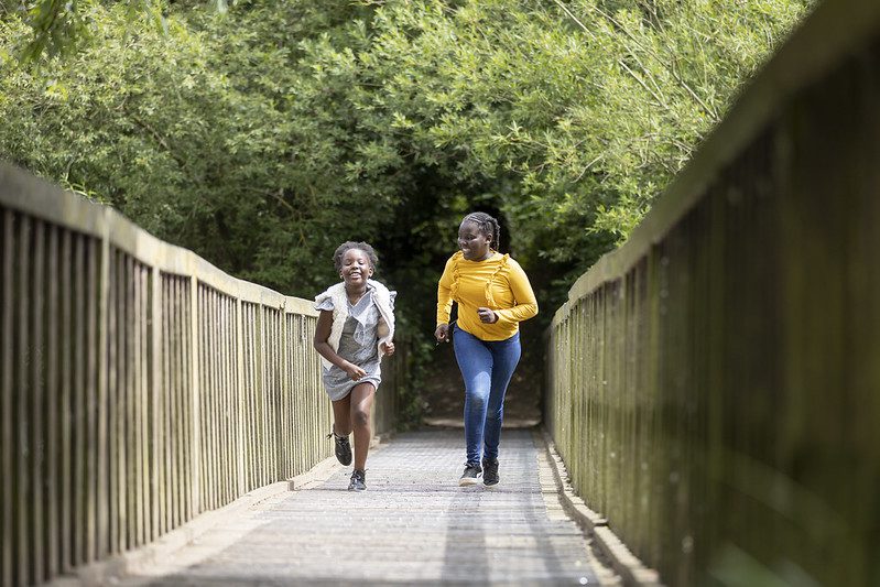 Two girls run across the bridge at Capstone Farm Country Park.
