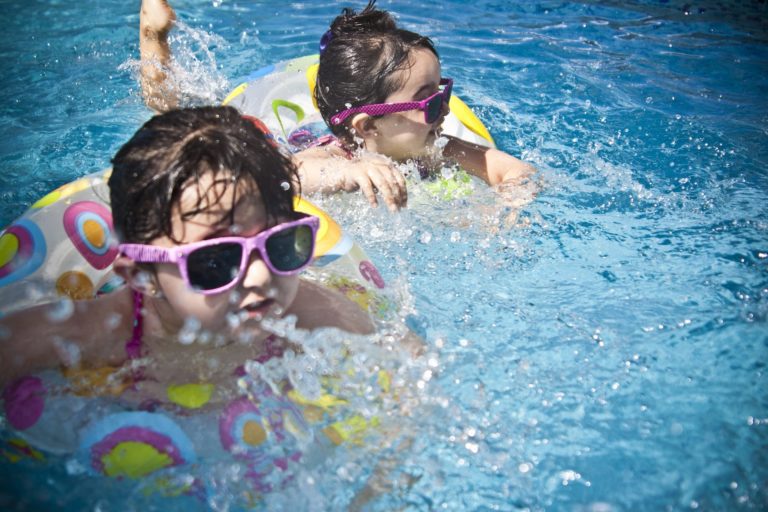 2 children swimming using rubber rings wearing pink sunglasses