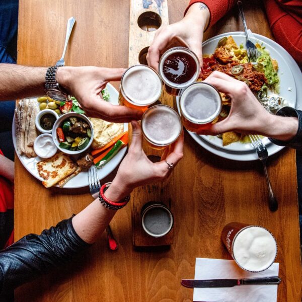 Close-up from above, four people with food on table at The Foundry Pub in Canterbury. Raising glasses.