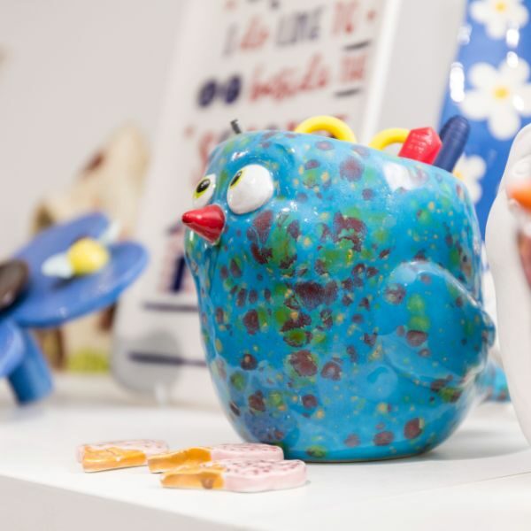 Close-up pottery vase, blue bird with red beak, with pens in opening at top.