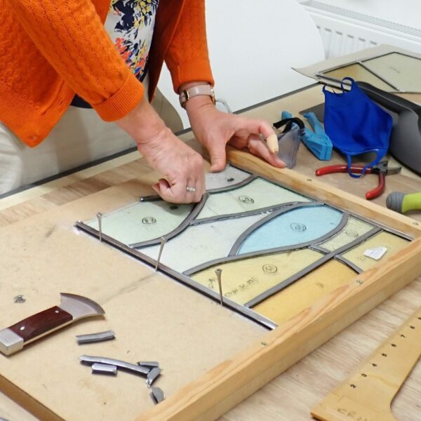 Close-up of person setting lead, in stain glass window.