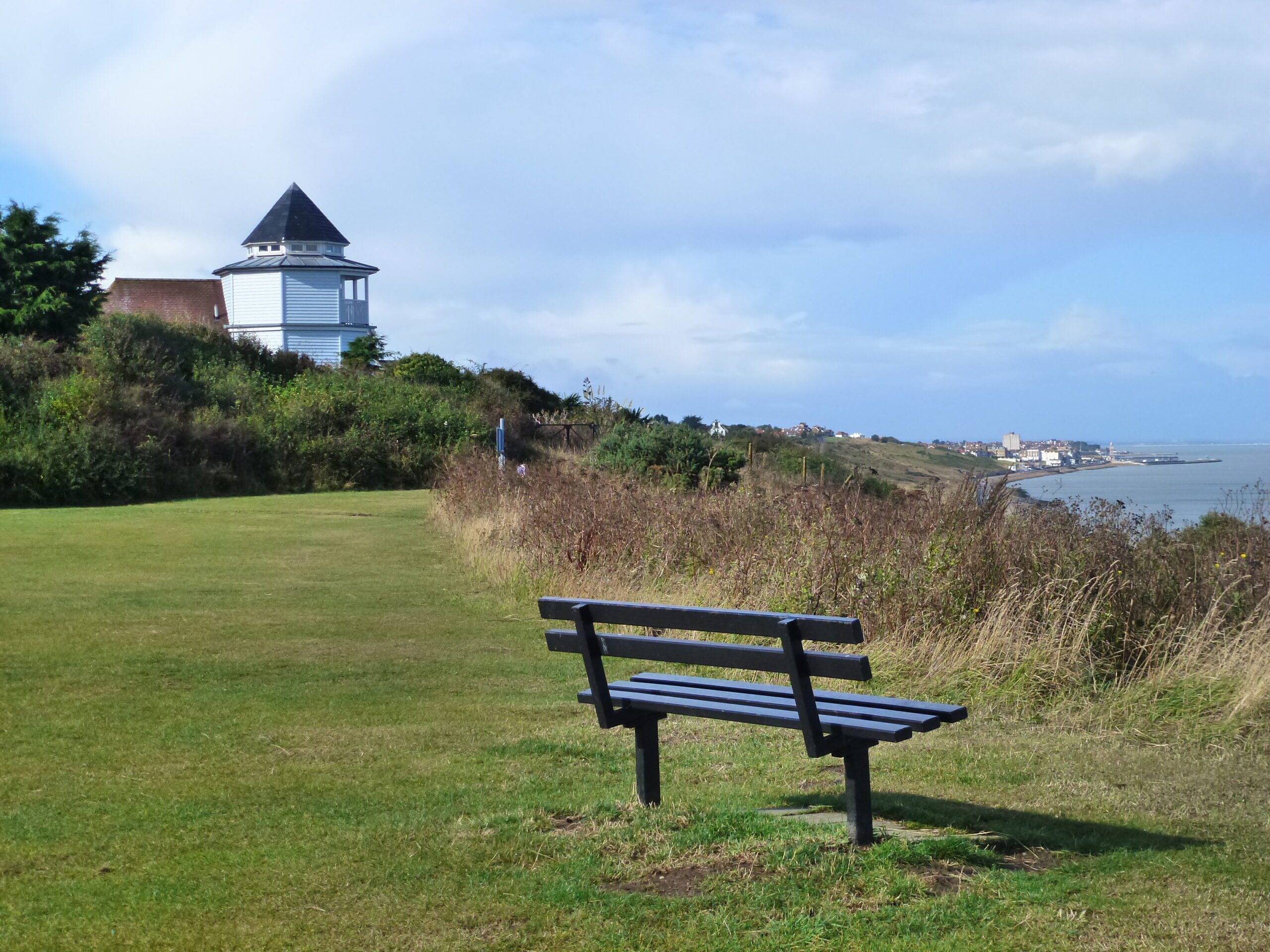 A bench looking at view of the sea. There is a white building in the background