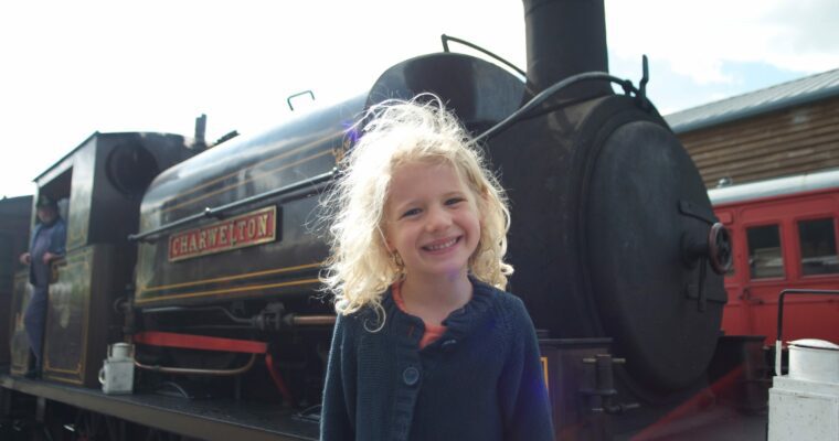 Image of a girl with blonde hair in front of a black steam train