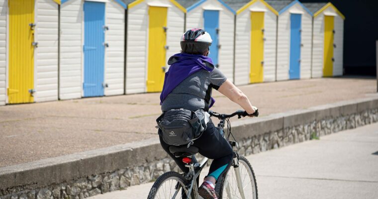 womens cycling past colurful beach huts at westgate on sea