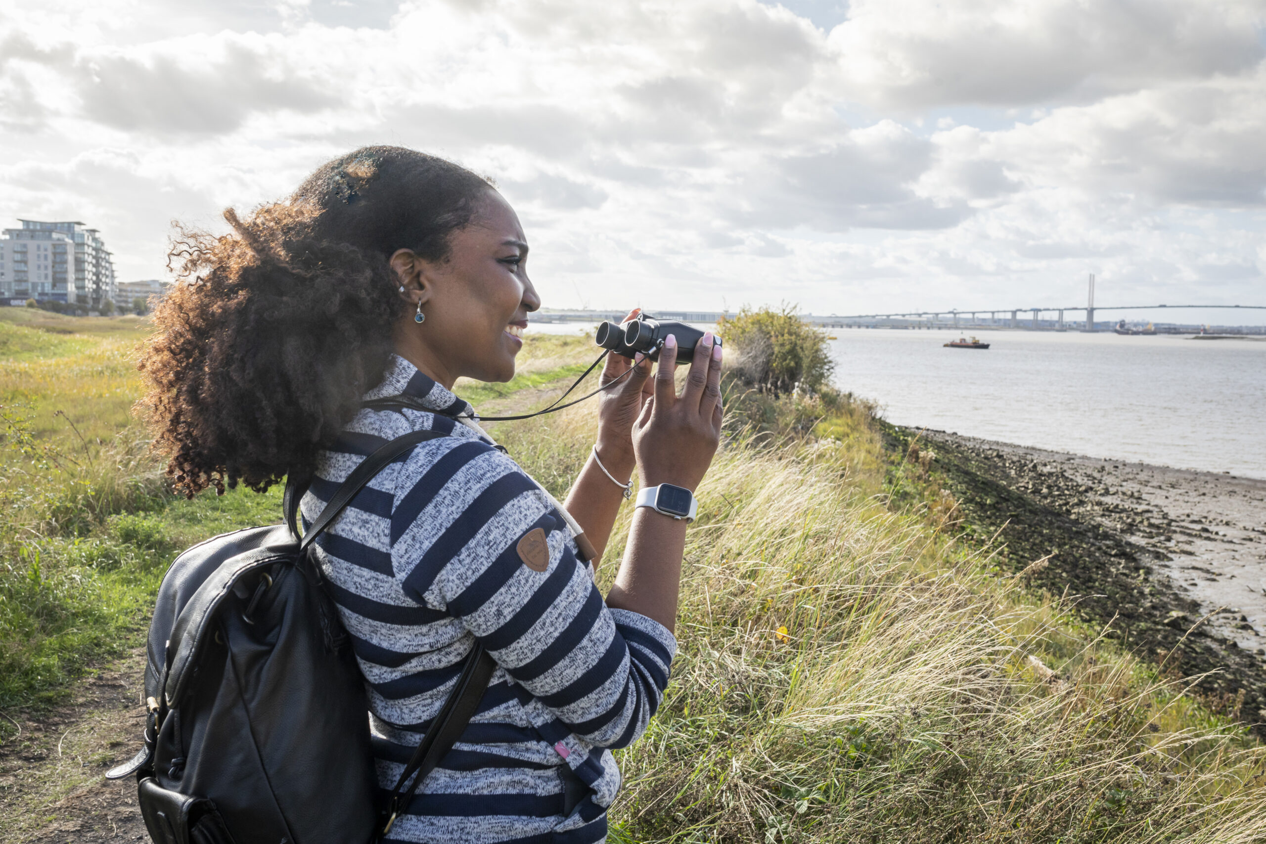 Female wearing a stripey top, using binoculars looking across Swanscome Peninsula