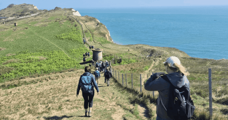 A group of walkers walking along the cliffs in Dover with the sea to their right