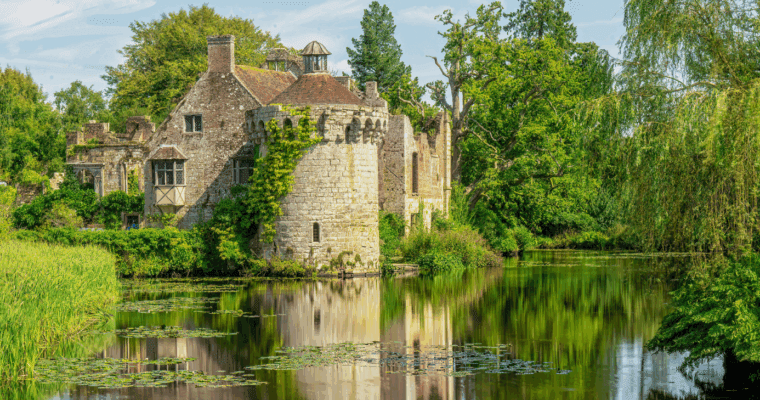 Old stone castle with a round tower, surrounded by trees and a calm moat.