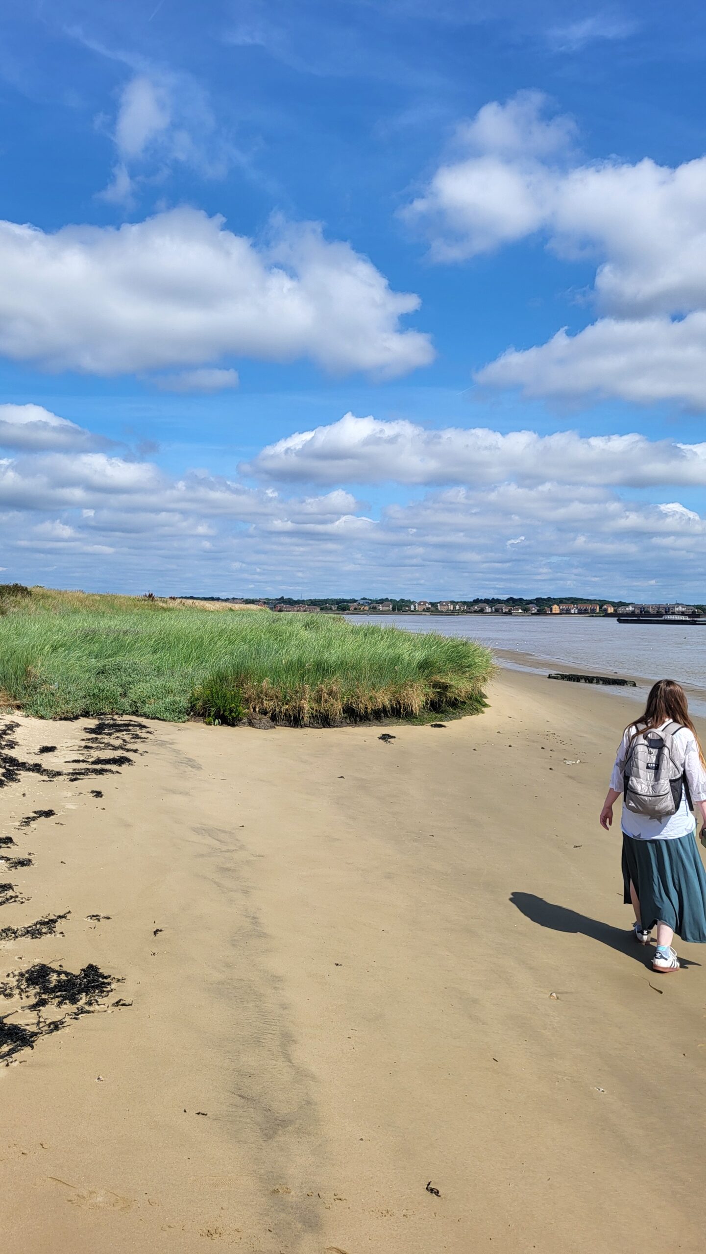Woman walking along Northfleet beach with a blue cloudy sky