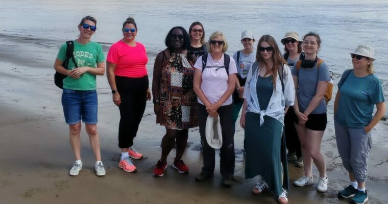 Group of women smiling at the camera standing on Northfleet beach. The River Thames is in the background.