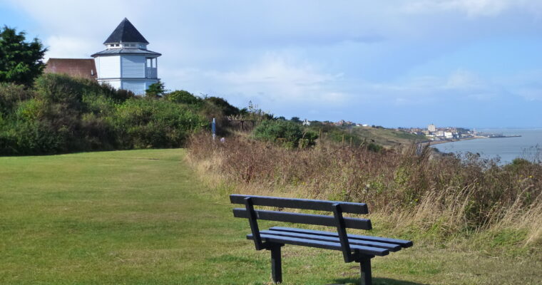 A bench looking at view of the sea. There is a white building in the background