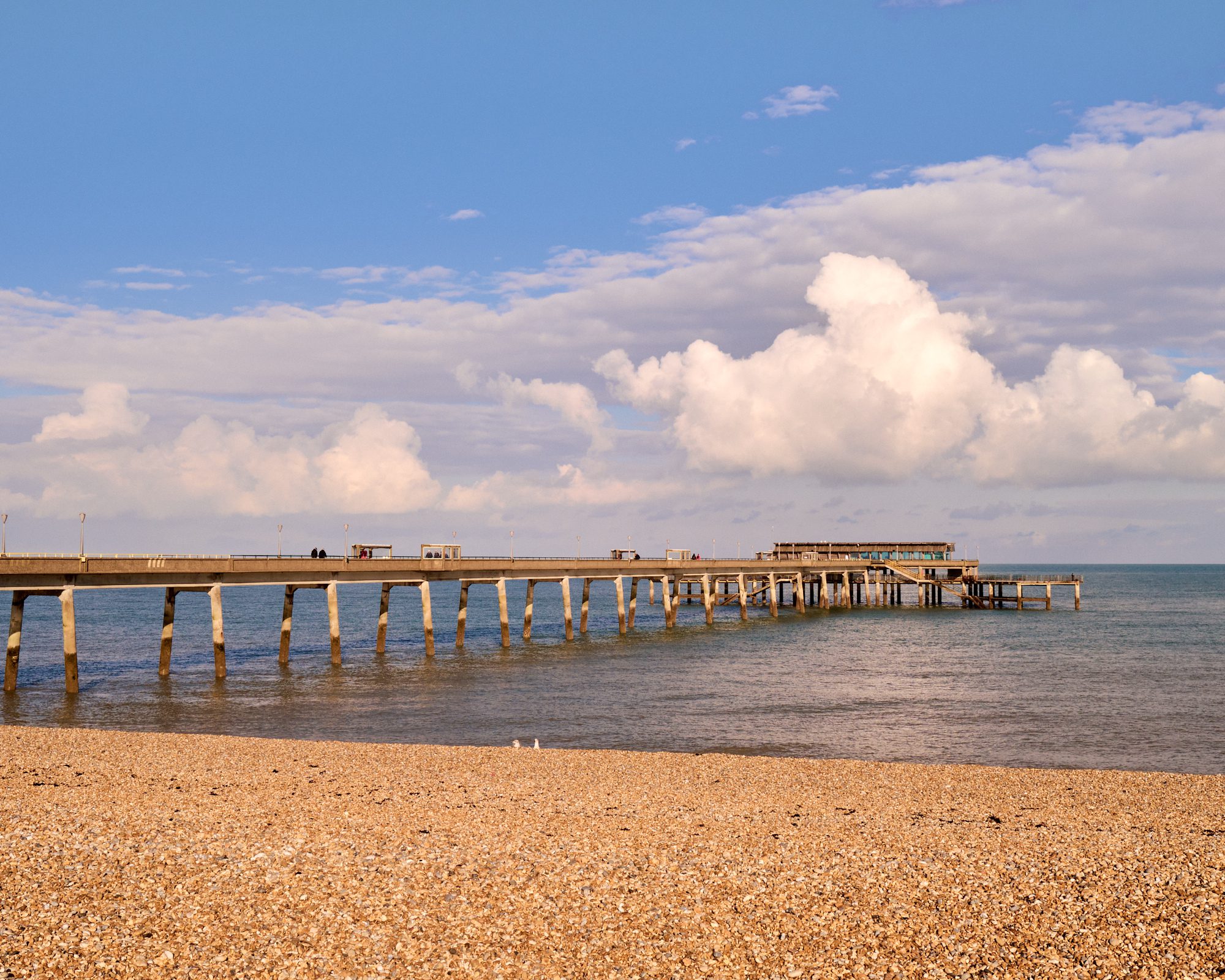 Deal Pier with a cloudy blue sky and a pebble beach