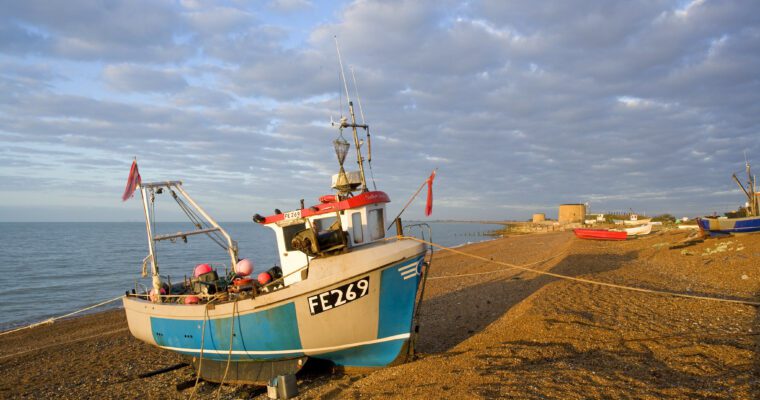 Fishing boat on a beach by the sea in Hythe, with Martello Towers in the background.