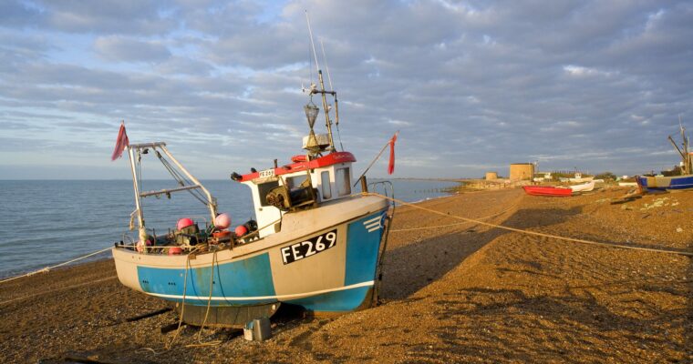 Fishing boat on a beach by the sea in Hythe, with Martello Towers in the background.