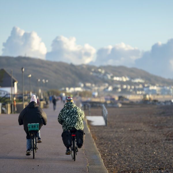 Two people on bikes cycling along the promenade in Hythe next to a shingle beach