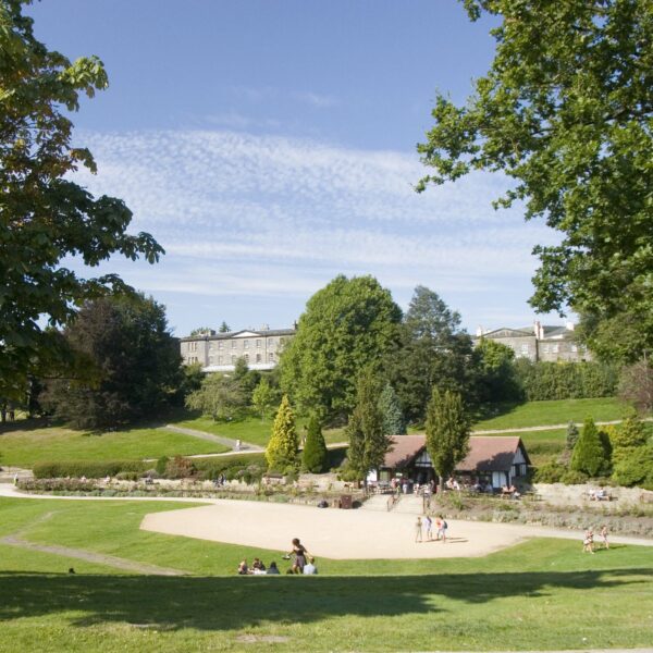 People sitting on the grass with a cafe and walking paths in the background in Calverley Park, Tunbridge Wells