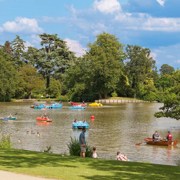 People in coloured boats on a lake surrounded by trees, Dunorlan Park