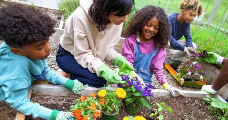 Mother and two children holding plants by plant bed
