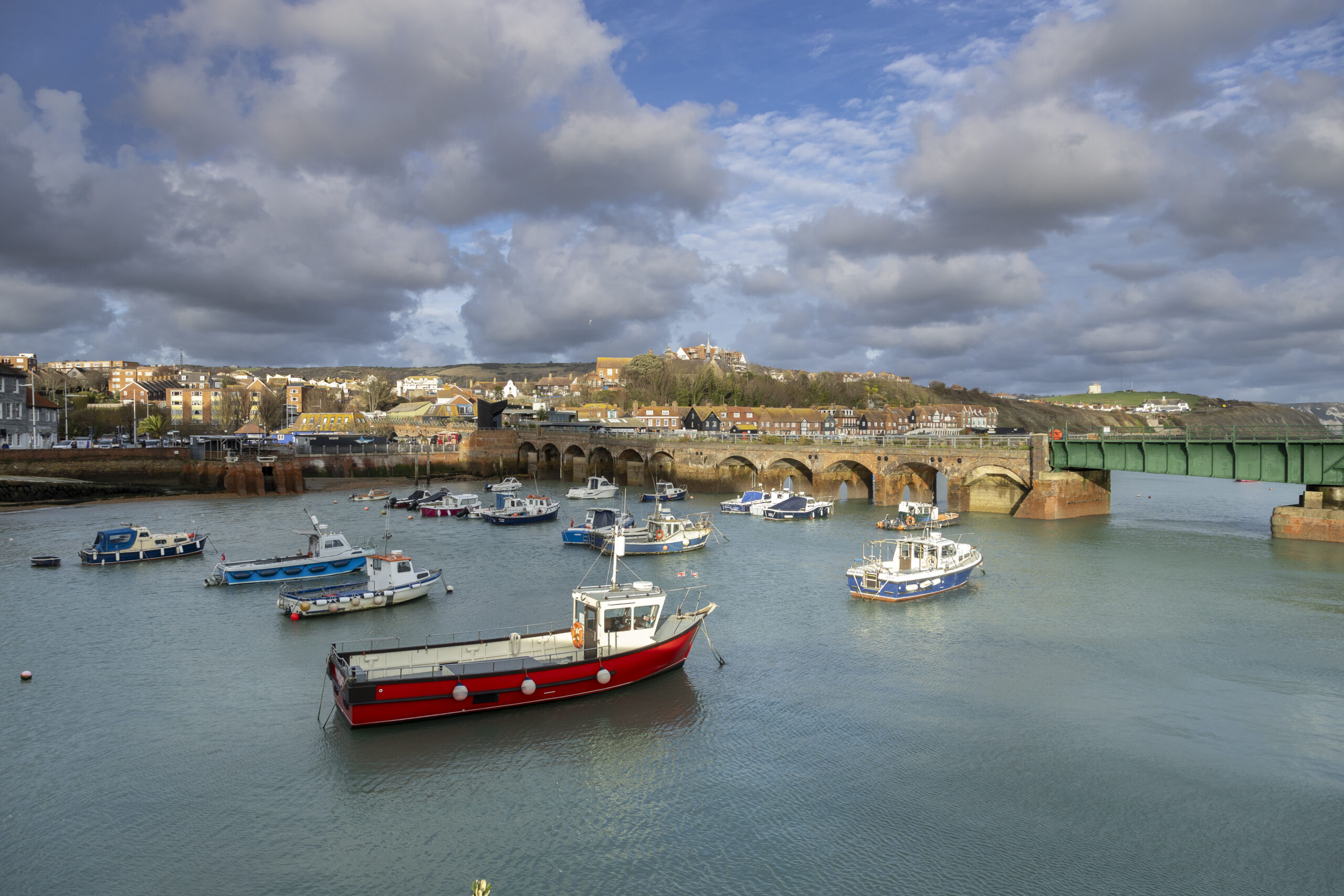Boats in the harbour, with a bridge in the background and a cloudy sky