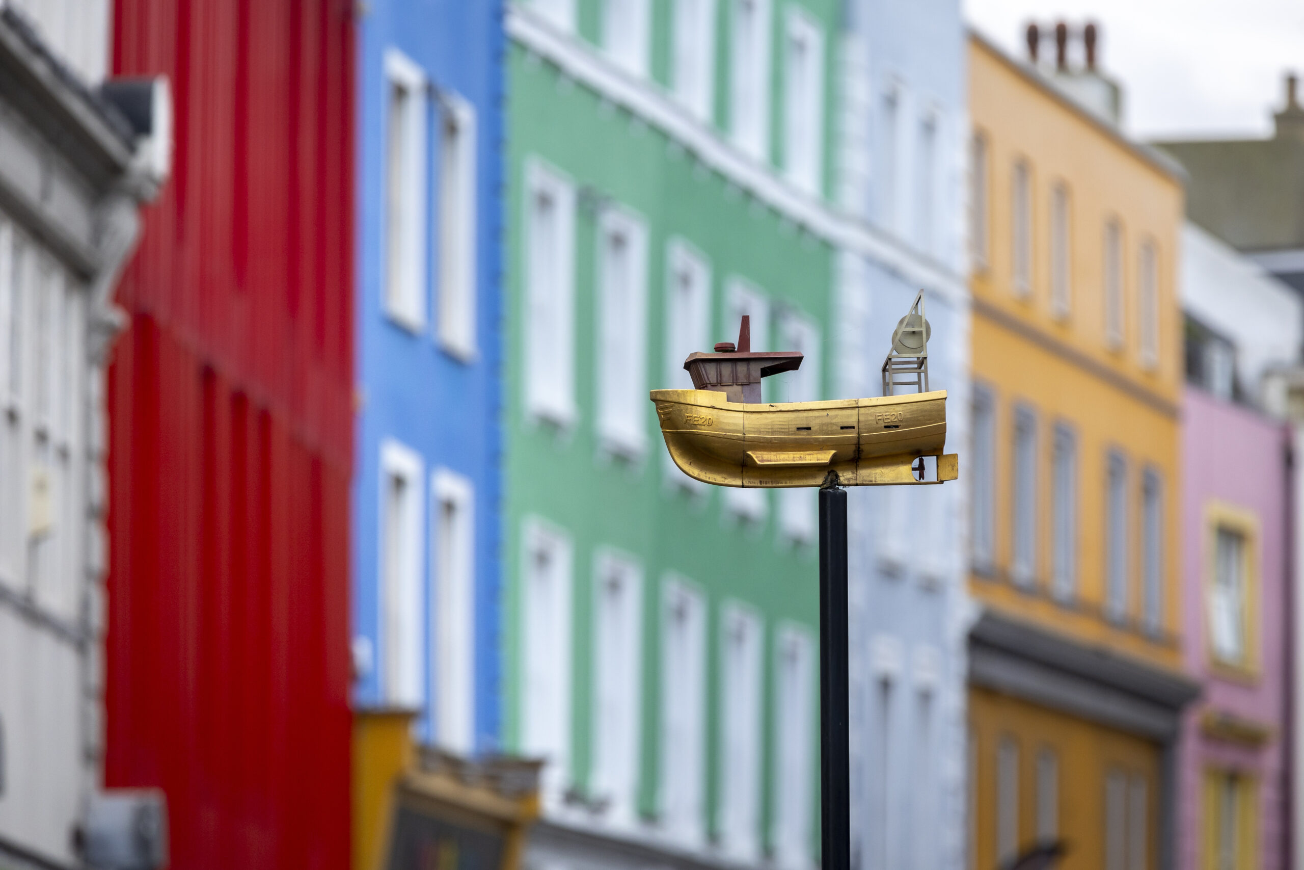 Blurred image of some colourful buildings. Focus is on a gold ornamental ship on a post.