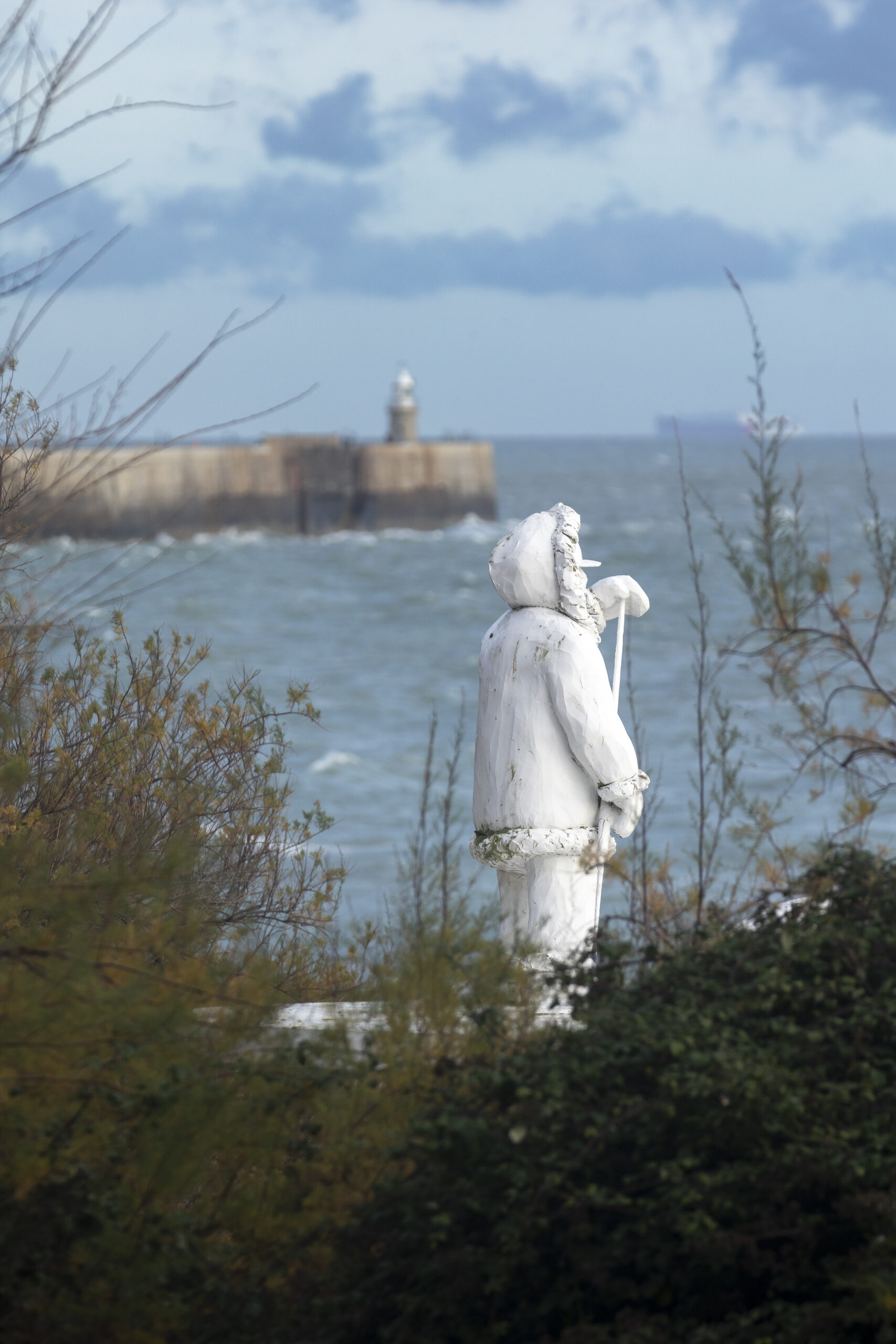 view out to sea from the park, there is a white statue of a man in the picture.
