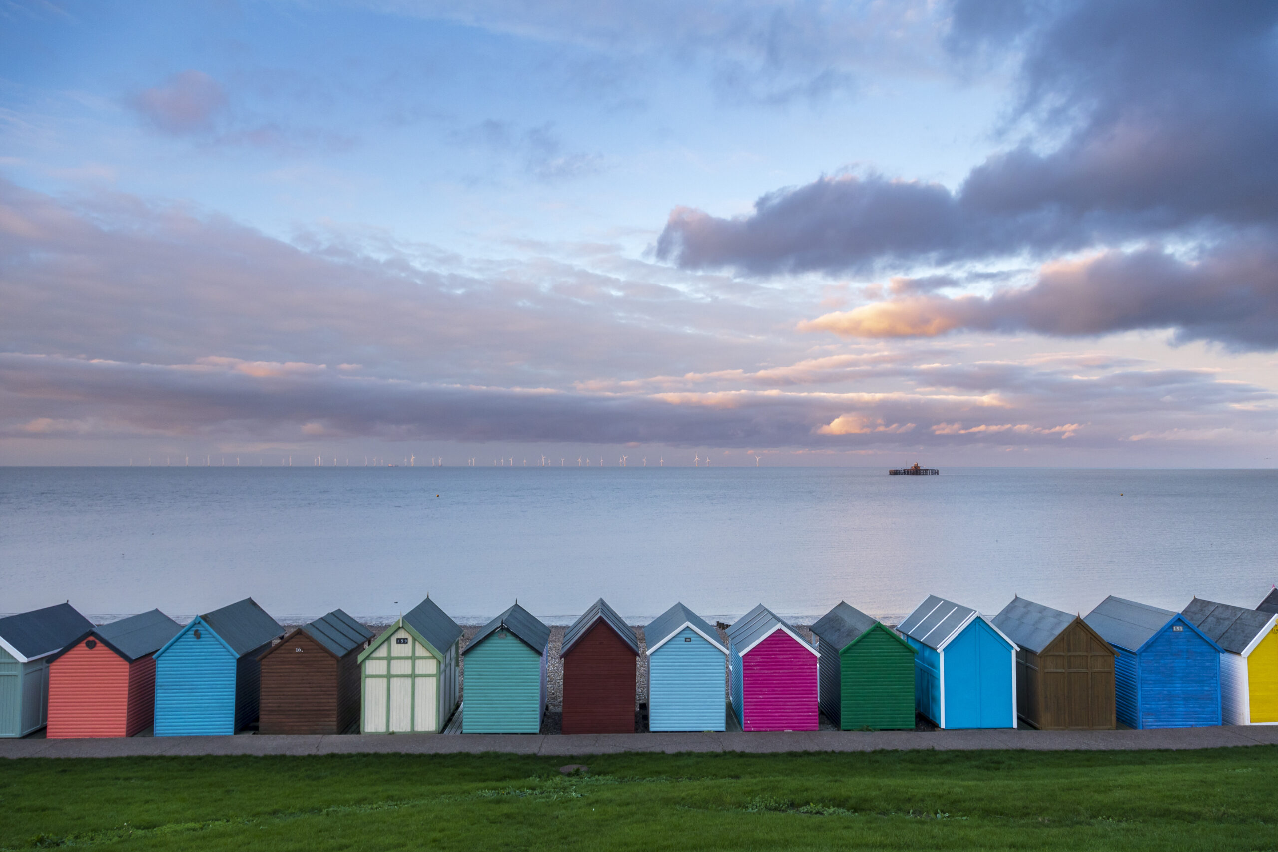 a view of the sea with colourful beach huts in front. The sky is pink and blue with clouds
