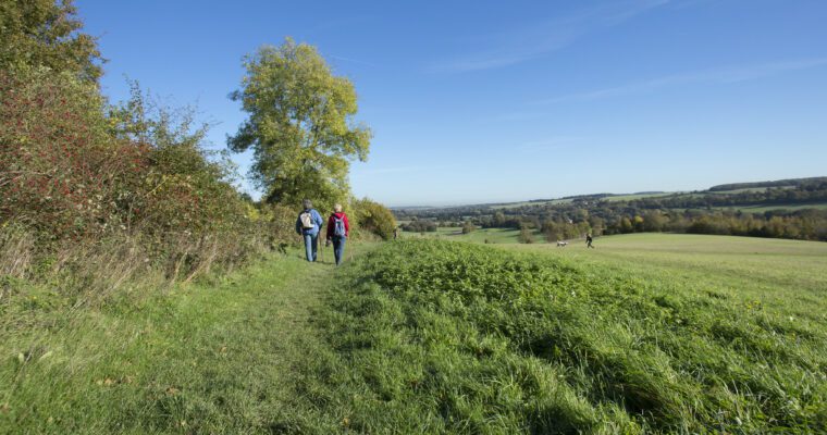 Two people walking on a grassy path with trees to the left and views of Darent Valley to the right, Lullingstone Country Park