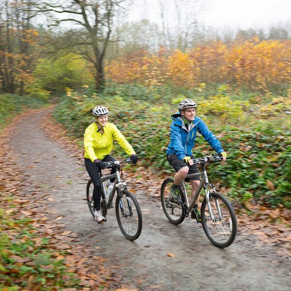 A man wearing a blue coat and a woman wearing a yellow coat cycling on bicycles in Bedgebury.