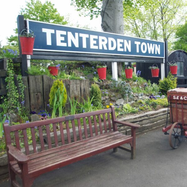 Large sign for Tenterden Town behind a bench on the platform at Tenterden Train Station.