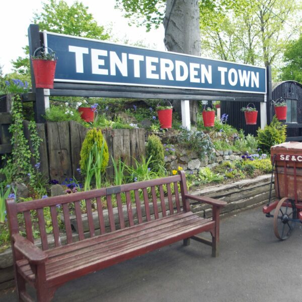Large sign for Tenterden Town behind a bench on the platform at Tenterden Train Station.