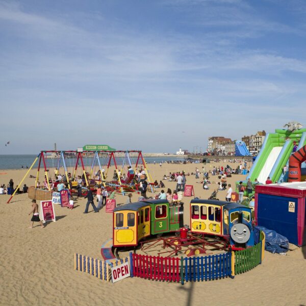 Children's attractions of swings, bouncy castles and a miniature train on a sandy beach next to the sea, Margate Main Sands.
