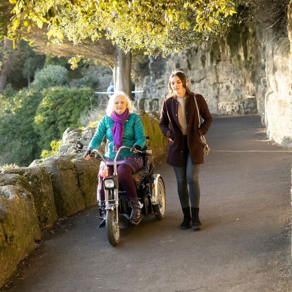 A woman walking next to another woman in a wheelchair down a slope, Lower Leas Coastal Park Folkestone