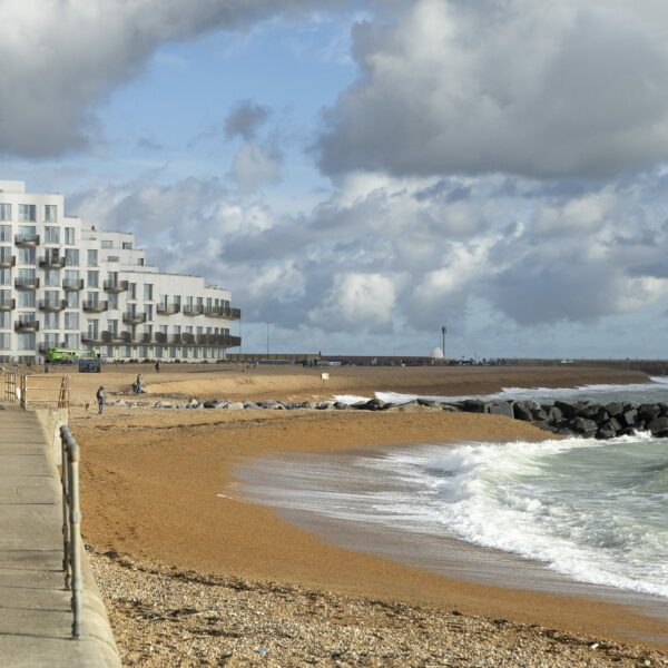 Two people walking along a hard-surfaced path next to the beach and sea