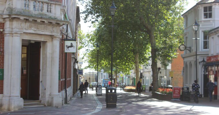 A street lined by buildings with people walking along it and trees.
