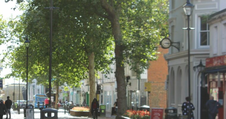 A street lined by buildings with people walking along it and trees.