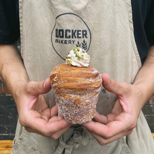 A person wearing a Docker Bakery apron holding a cruffin - a cross between a croissant and a muffin