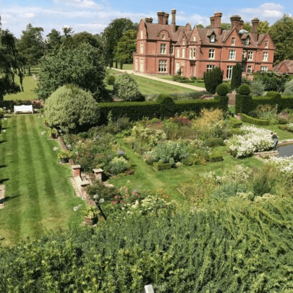 View looking down on formal gardens with a manor house in the background.