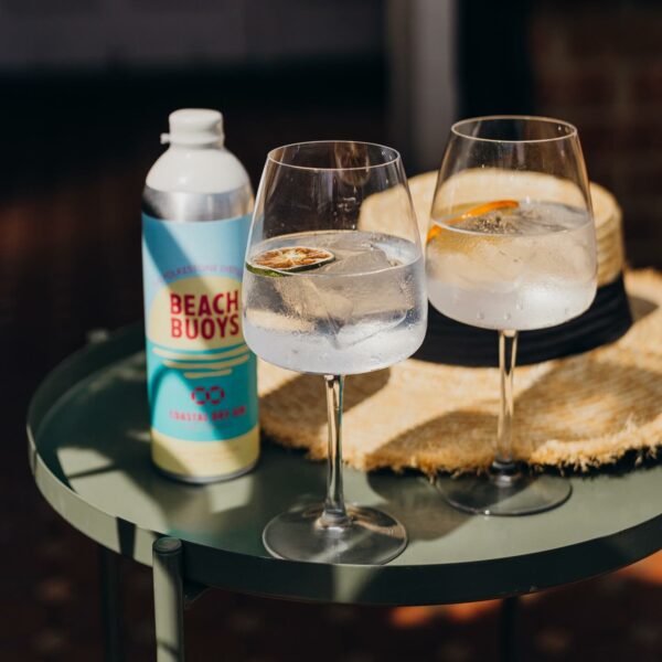 Two glasses of gin on a table next to a bottle of Folkestone Distillery Gin with a straw hat in the background.