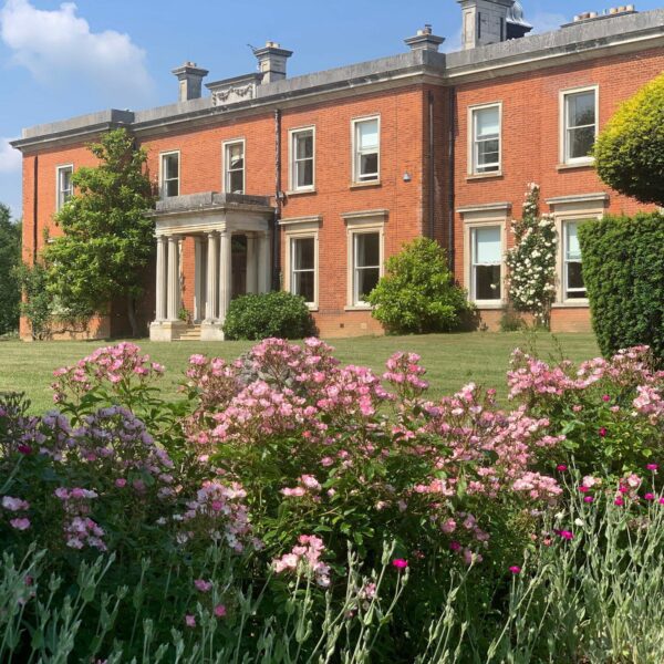 Manor house overlooking a garden with pink flowers and shrubs.