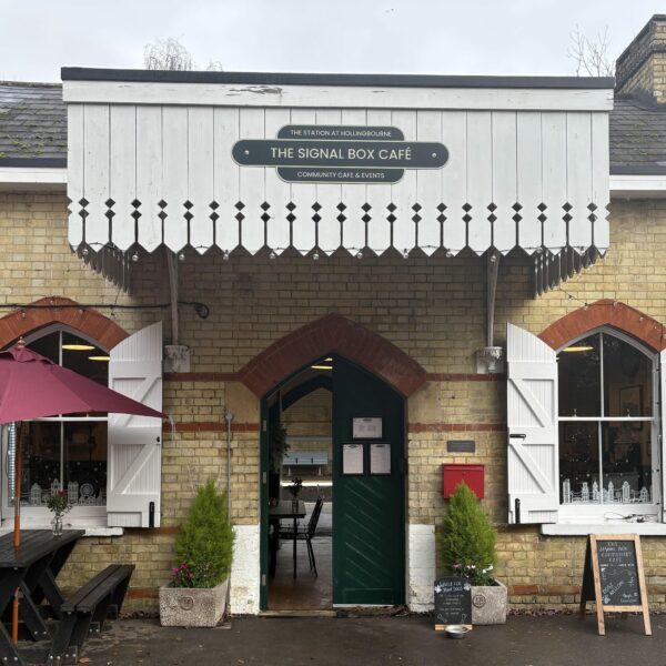 The outside of a railway station ticket office with a bench and plants outside.