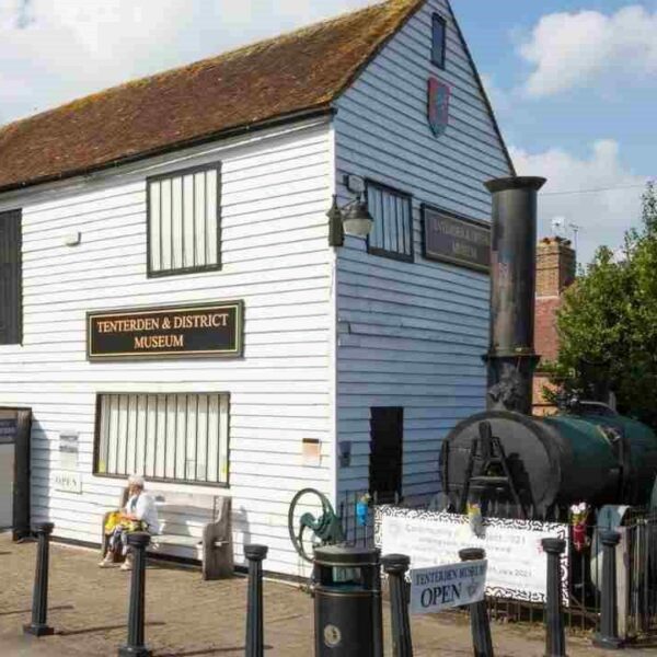 A white building with people stood outside and a model of a train next to it.