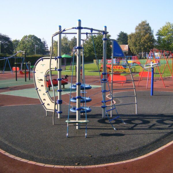 Colourful climbing frames and swings in a children's playground with a grass field in the background.