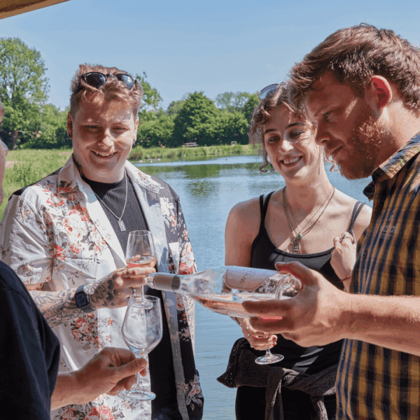 A man pouring wine into a glass while two people watch on, during a wine tasting at Wildshark Vineyard.