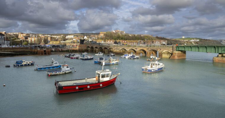 Boats in the harbour, with a bridge in the background and a cloudy sky