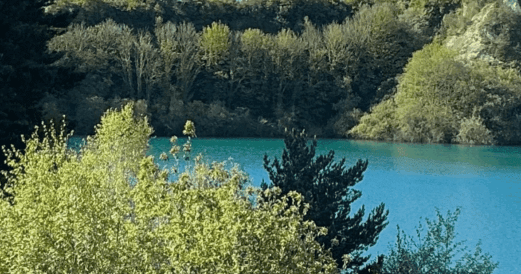 Turquoise lake surrounded by green trees and hills.